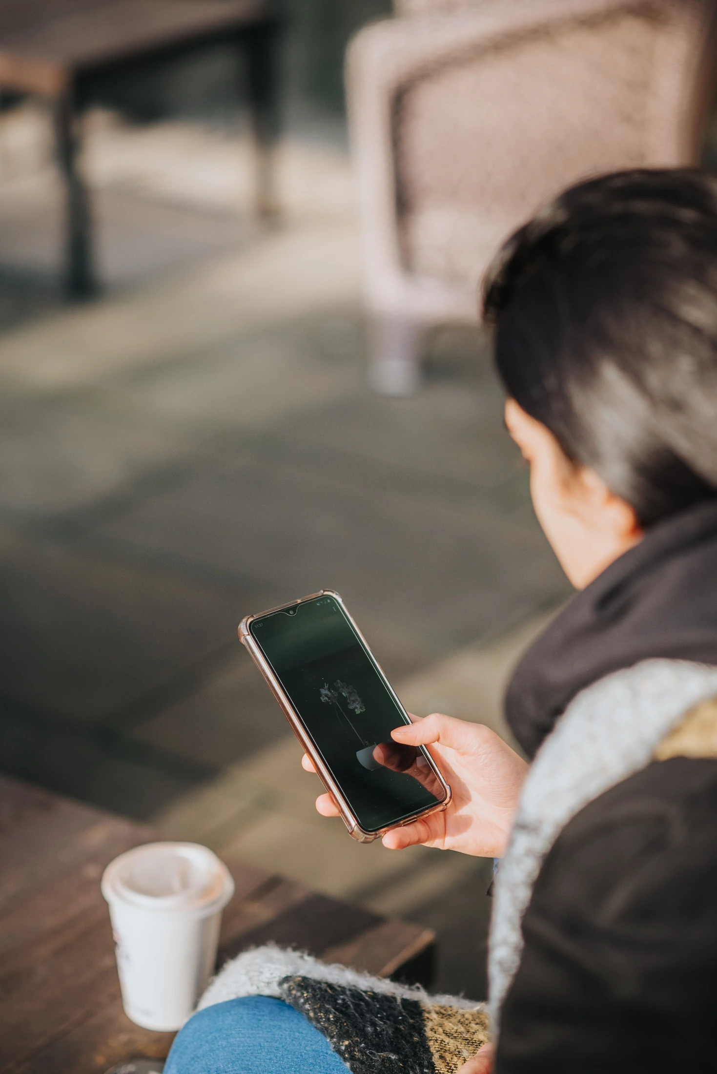 A café guest using a smartphone beside a takeaway coffee