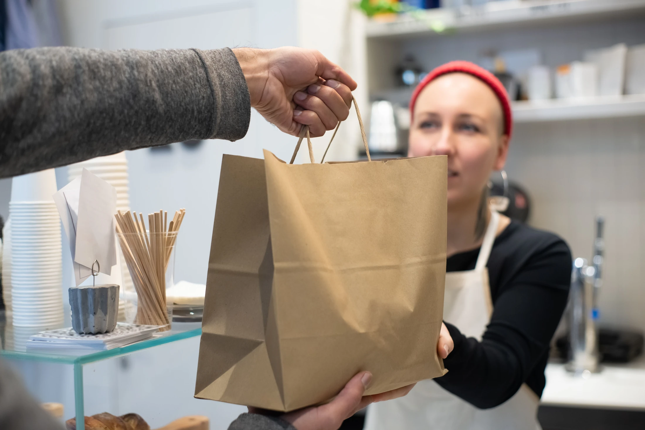 A cafe team member handing a takeaway bag to a customer